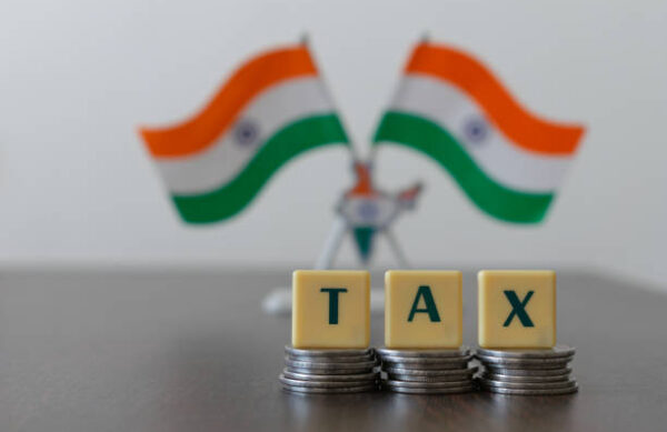 Mumbai, India - 26 January 2022, Letter blocks arranged as 'TAX' on pile of coins and blur Indian flag Tricolor in the background.  Main focus is on letter blocks and coins. Government schemes concept